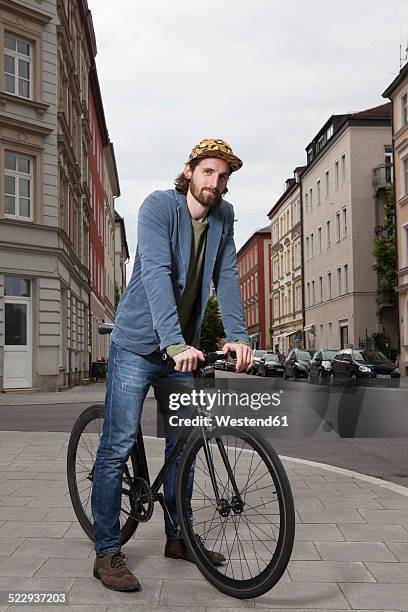 germany, bavaria, munich, young man wearing basecap standing on pavement with his racing cycle - rue 21 photos et images de collection