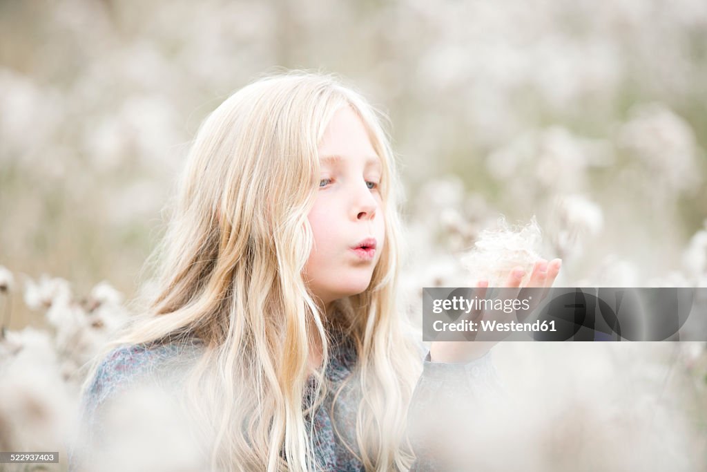 Portrait of girl standing in a field blowing seeds out off her hand