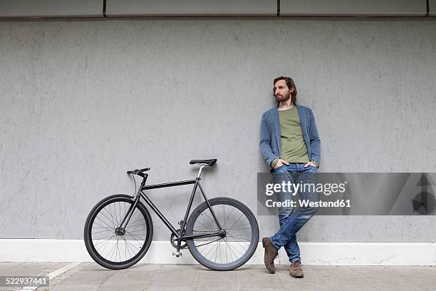germany, bavaria, munich, young man standing besides his racing cycle leaning on a wall - leunen stockfoto's en -beelden