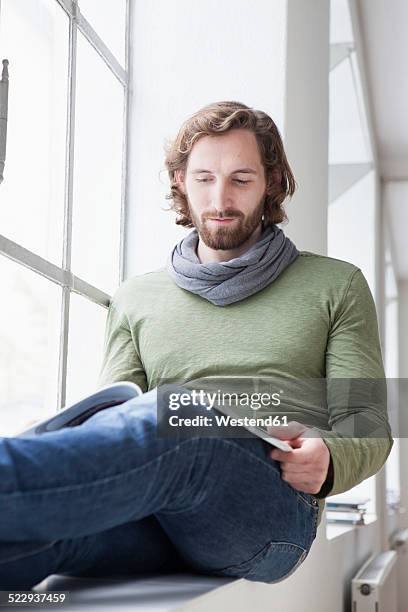 portrait of young man with magazine sitting on window sill in an office - münchen immobilie büro stock-fotos und bilder