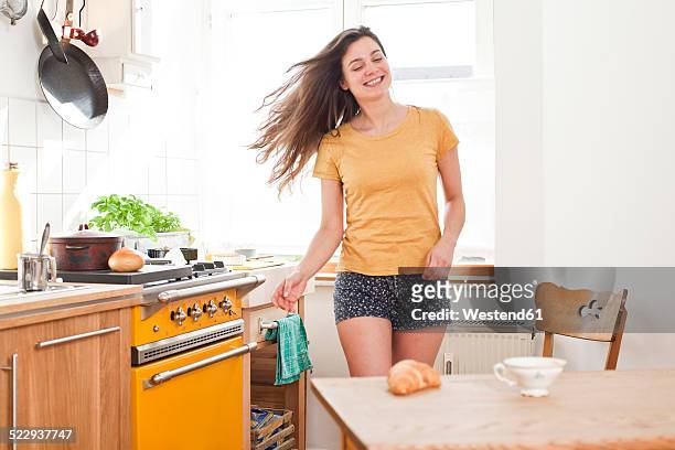 portrait of smiling young woman dancing in her kitchen - haare schütteln stock-fotos und bilder