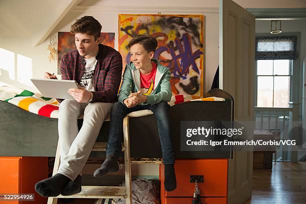 brothers sitting on bunkbed with digital tablet, abstract paintings on wall, door open - 二段ベッド ストックフォトと画像