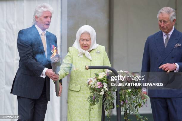 Pageantmaster Bruno Peek hands Britain's Queen Elizabeth II a torch for her to light the first beacon in honour of her 90th birthday in Windsor on...