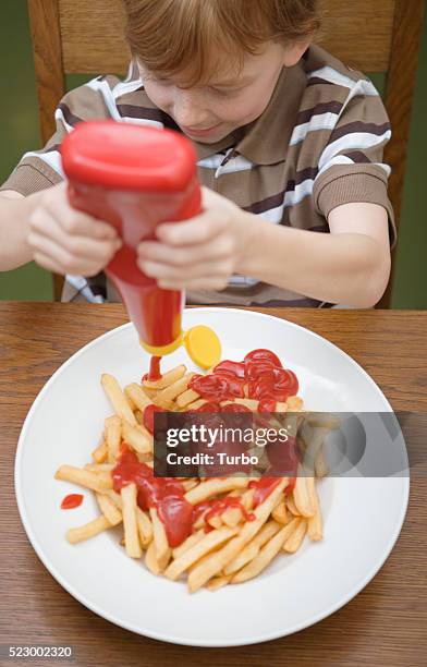 boy eating french fries with ketchup - squirt stockfoto's en -beelden