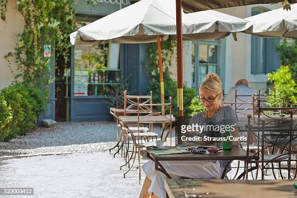 woman enjoying her tablet reader while seated in outdoor cafe. - frans terras stockfoto's en -beelden