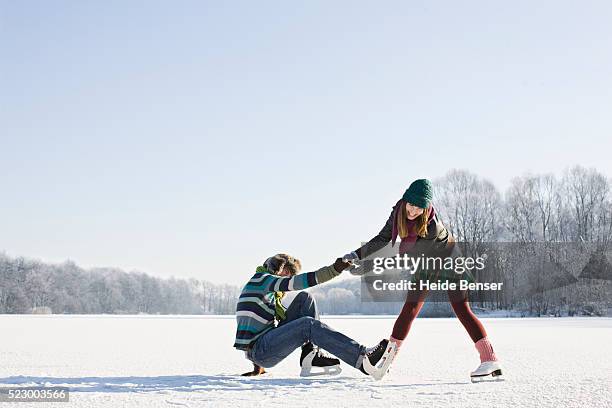 woman helping up fallen man - アイススケート ストックフォトと画像