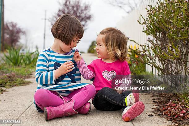 two girls (2-3, 4-5) sitting on sidewalk with flowers - aufteilung stock-fotos und bilder