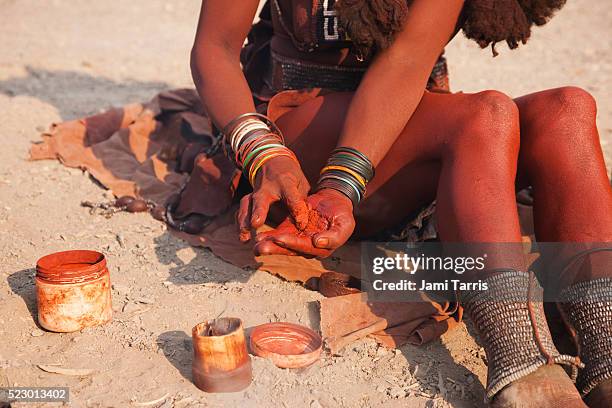 a himba girl mixes ochre and fat to apply to her exposed skin - himba stock-fotos und bilder