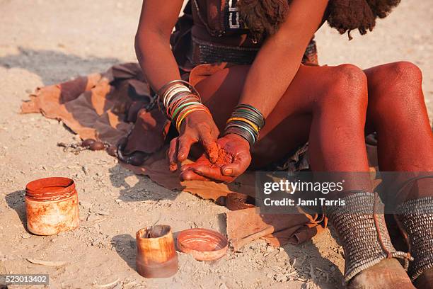 a himba girl mixes ochre and fat to apply to her exposed skin - himba imagens e fotografias de stock