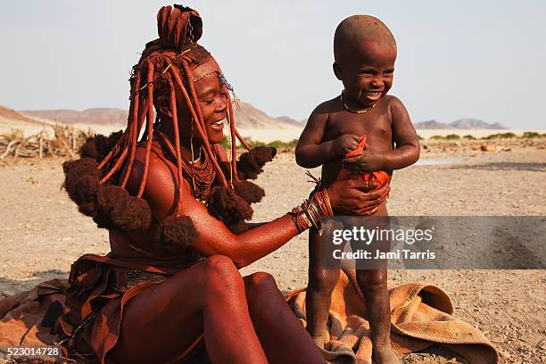 a himba woman mixes ochre and fat to apply to exposed skin and hair for beauty and sun protection - himba stock-fotos und bilder