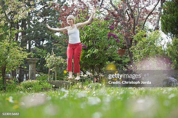 young woman balancing on a rope in a garden - woman tightrope stock pictures, royalty-free photos & images