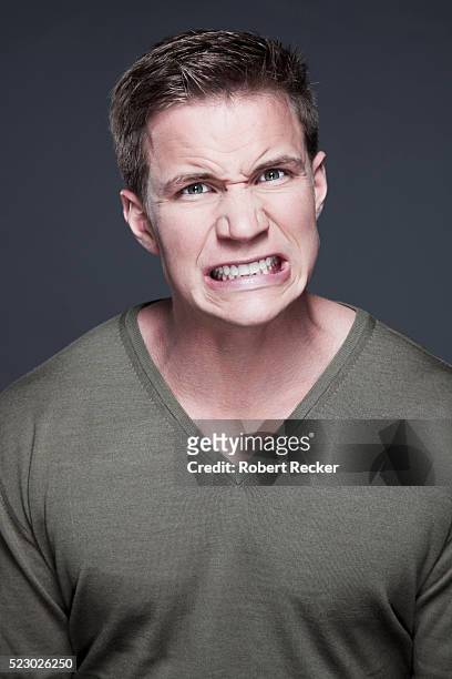 studio portrait of young man clenching teeth - serrare i denti foto e immagini stock