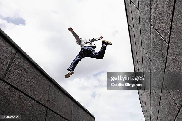 teenage boy (16-16) jumping over gap between walls - le parkour fotografías e imágenes de stock