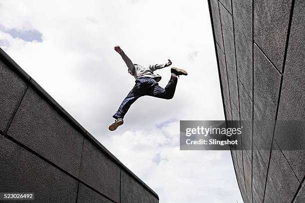 teenage boy (16-16) jumping over gap between walls - jumping imagens e fotografias de stock