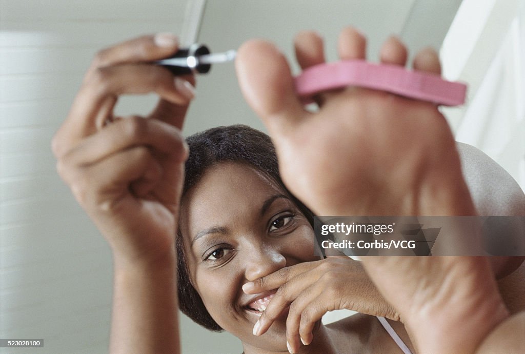 Young Woman Applying Nail polish to Her Toenails