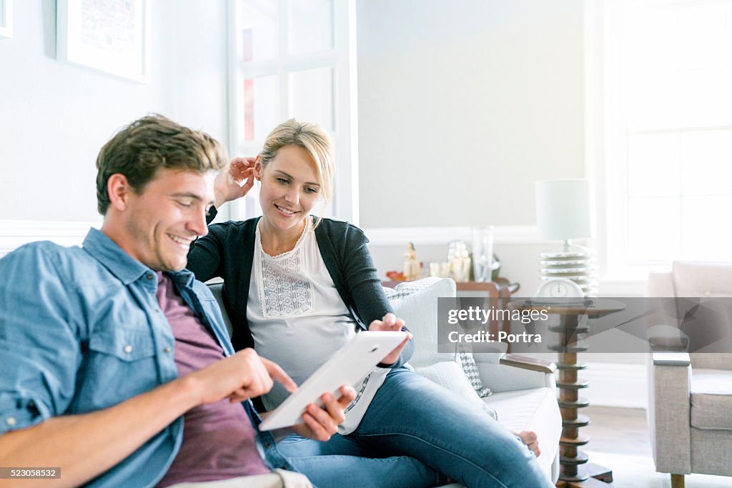 Casal feliz usando Tablet digital com sofá