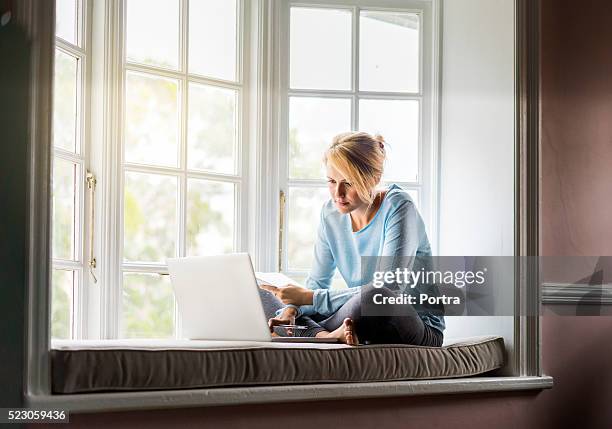 junge frau benutzt laptop auf fensterbank - mobile stock-fotos und bilder