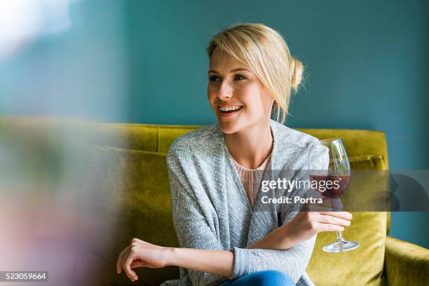 felice donna che tiene bicchiere di vino rosso su un divano - blonde glasses foto e immagini stock