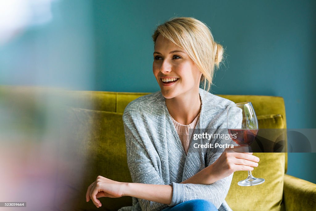 Happy woman holding glass of red wine on sofa