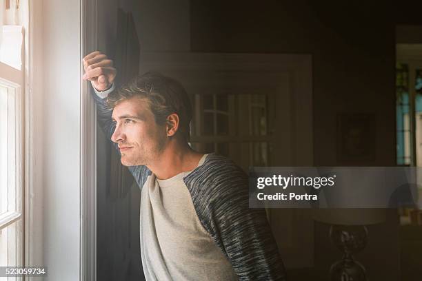 thoughtful man looking through window at home - man looking through window stock pictures, royalty-free photos & images