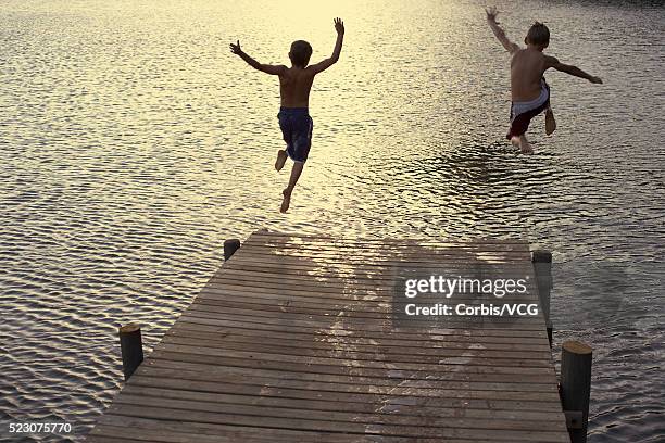 two boys diving off dock into lake - group-of-friends-jumping-off-dock-into-lake stock pictures, royalty-free photos & images