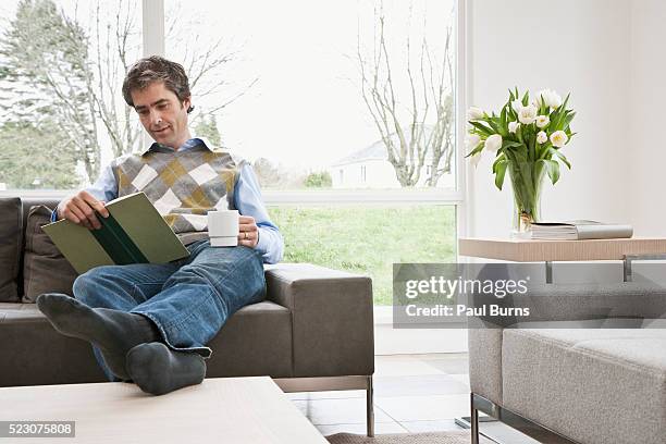 man reading book on sofa with feet up - coffee table reading mug stock pictures, royalty-free photos & images