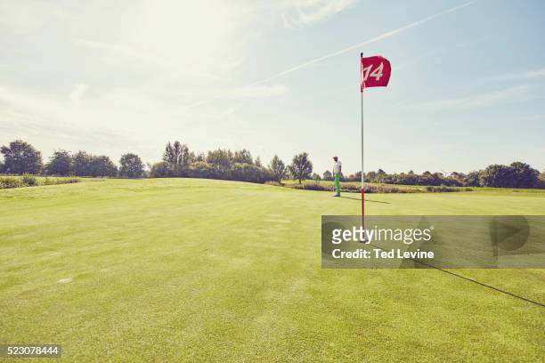 view of golf flag with golfer in background - golfvlag stockfoto's en -beelden