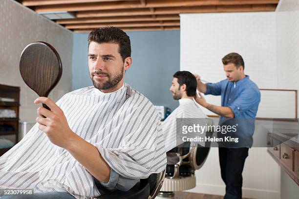 customer admires haircut in mirror - busy barber shop stock pictures, royalty-free photos & images