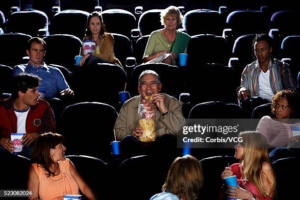 mature man eating potato chips in movie theater auditorium - clueless movie stock-fotos und bilder