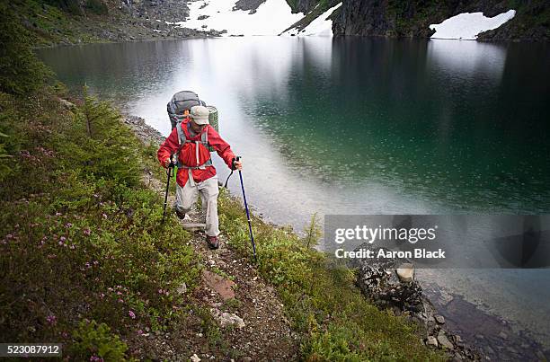 man in red jacket with backpack hiking beside turquoise lake - the old strathcona stock pictures, royalty-free photos & images