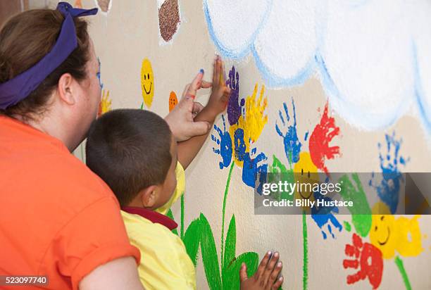 kindergarten teacher helps a young boy paint a colorful mural using his handprint. - child care worker stockfoto's en -beelden