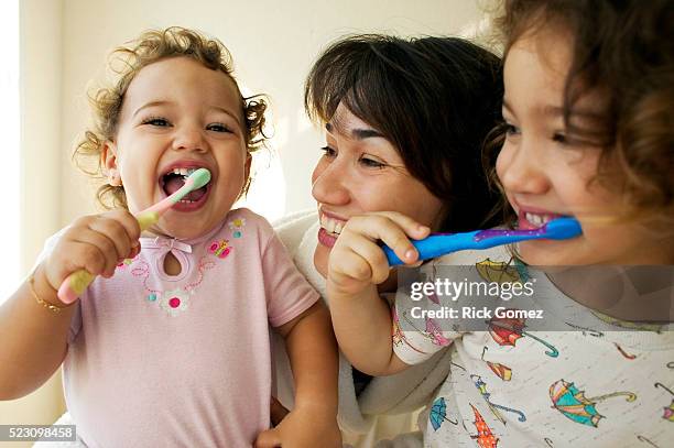 mother helping daughters brush teeth - tandpasta stockfoto's en -beelden