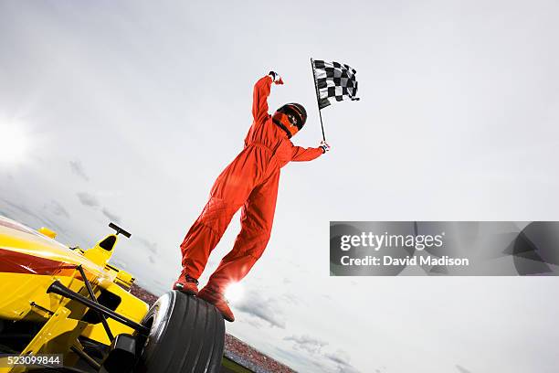 driver standing on racecar holding checkered flag - piloto de carro de corrida imagens e fotografias de stock