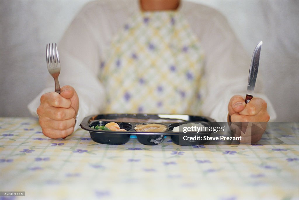 Man with Knife and Fork Sitting next to TV Dinner