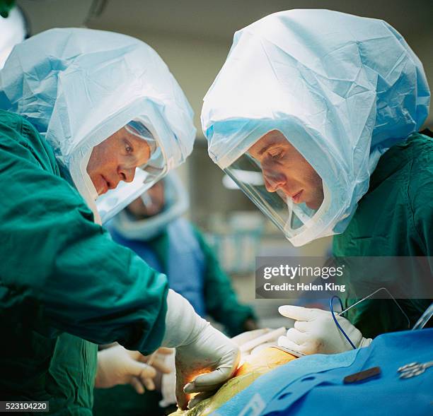surgeons in clean suits during operation - white suit stock pictures, royalty-free photos & images