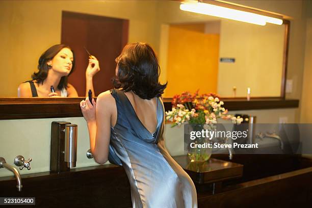 woman applying makeup in bathroom mirror - woman cocktail dress stock pictures, royalty-free photos & images