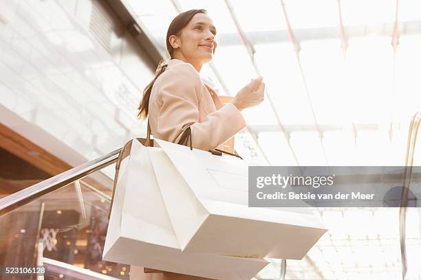 woman standing on escalator holding shopping bags - shopping mall fotografías e imágenes de stock