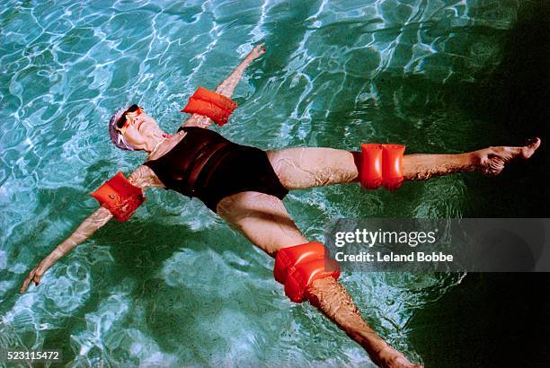 senior woman floating in swimming pool - armband stock pictures, royalty-free photos & images