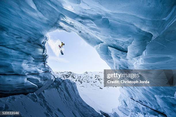 male snowboarder jumping down from a glacier cave - snow boarding stock-fotos und bilder