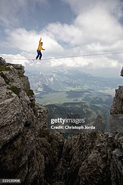 young man balancing on high rope between two rocks in mountains, alps, tyrol, austria - equilibrist stock pictures, royalty-free photos & images