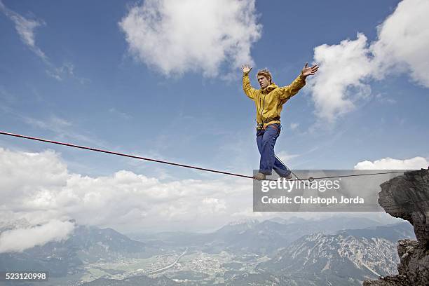 young man balancing on high rope between two rocks in mountains, alps, tyrol, austria - tightrope stockfoto's en -beelden