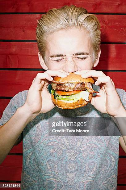 young man eating large hamburger - burgers stockfoto's en -beelden