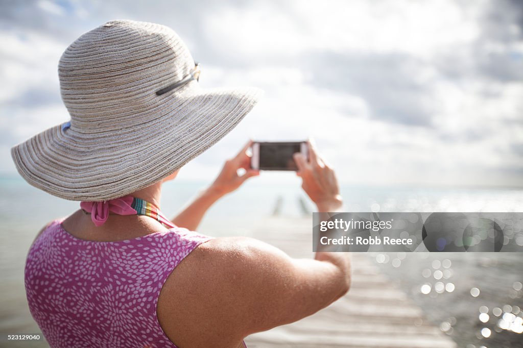 A woman on vacation, photographing the ocean with a smartphone.