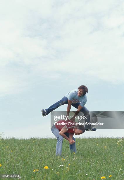 two men playing leapfrog in meadow - bockspringen stock-fotos und bilder