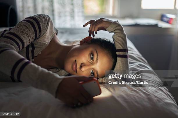 teen (16-17) girl lying on bed using smartphone - bed phone stock-fotos und bilder