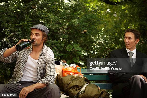 businessman and homeless man sitting on park bench - social inequality stock pictures, royalty-free photos & images