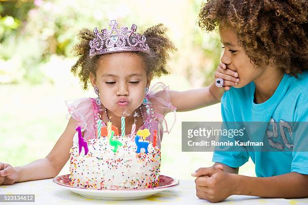 girl blowing out birthday candles and holding brother's mouth - happy birthday crown foto e immagini stock