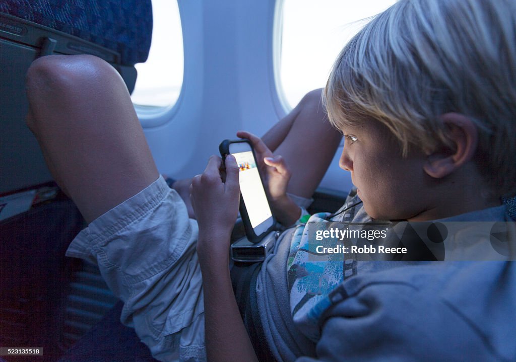 A young boy sitting in an airplane looking at a smartphone