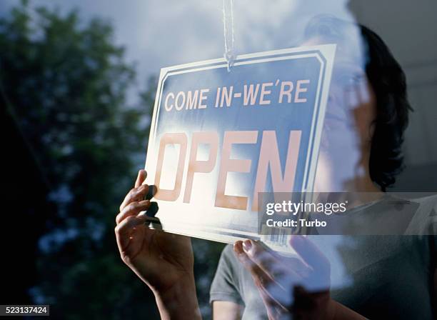 woman holding "come in we're open" sign - open sign stock pictures, royalty-free photos & images