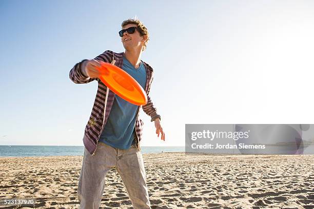 man on beach tossing frisbee - frisbee stock-fotos und bilder